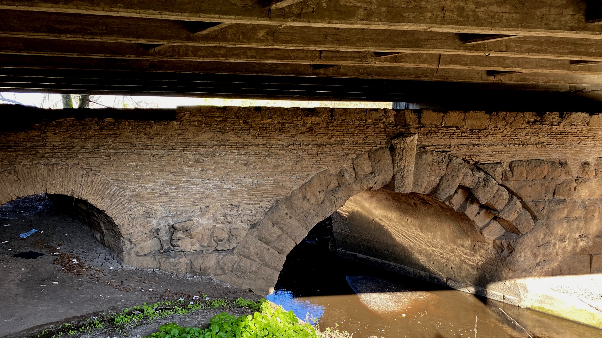 Two arches of an old Roman bridge hidden under the carriageway of a large modern road