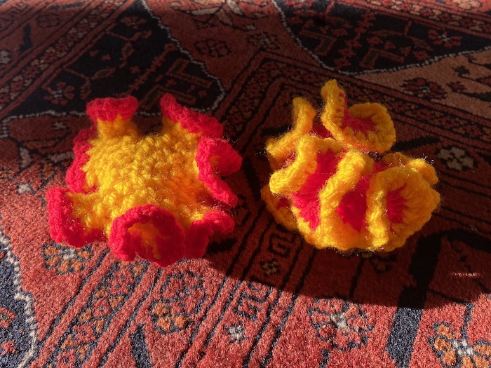 Two crocheted hyberbolic surfaces on a Turkish rug. One is yellow with a red border and looks something like a nudibranch, or seaslug. The other is red with a yellow border and is more convopluted, like a brain coral.