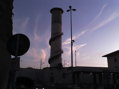 The spiral staircase around a big chimney outside Termini station in Rome silhouetted against a sky with wispy clouds