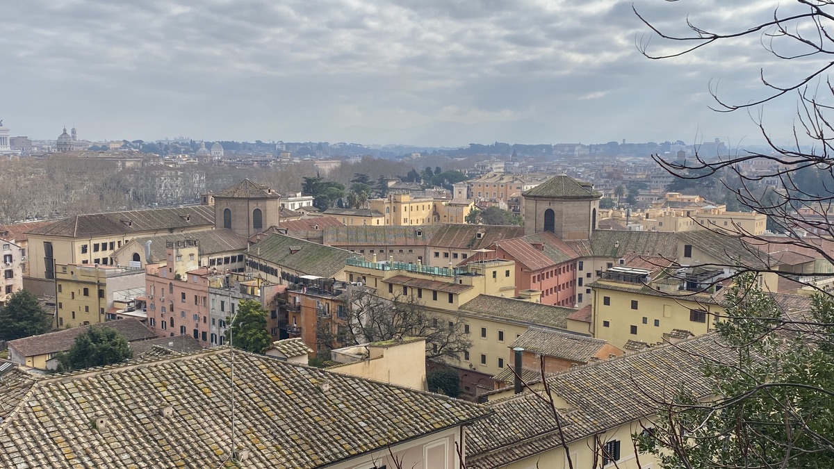 A view of the Regina Coeli prison from the Janiculum hill. There are two panopticon-type towers and the quest is near the one on the left. Behind is the urban landscape of Rome and overcast skies.
