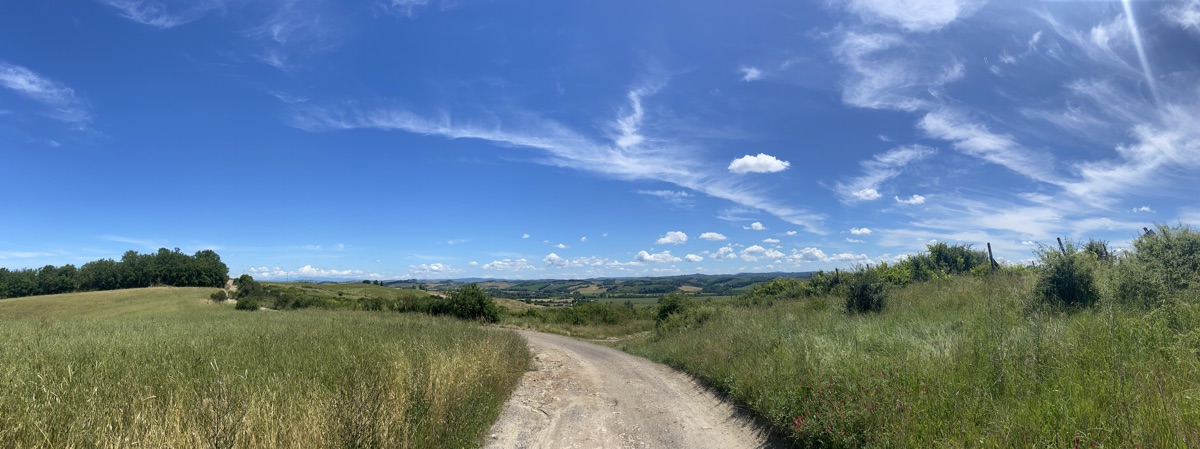 Panoramic view of rolling Tuscan hills under a blue sky with fluffy white clouds