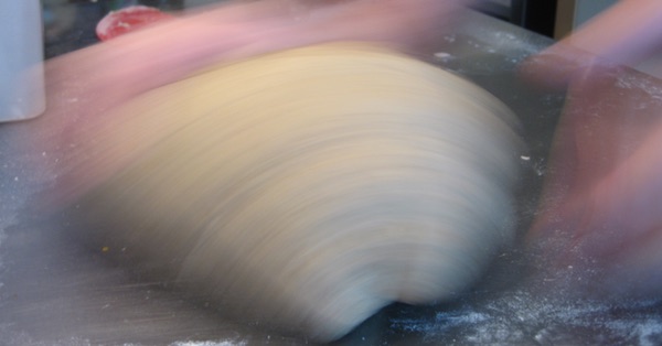 Two hands kneading a ball of dough shot with a slow shutter speed so that the hands and dough are blurred